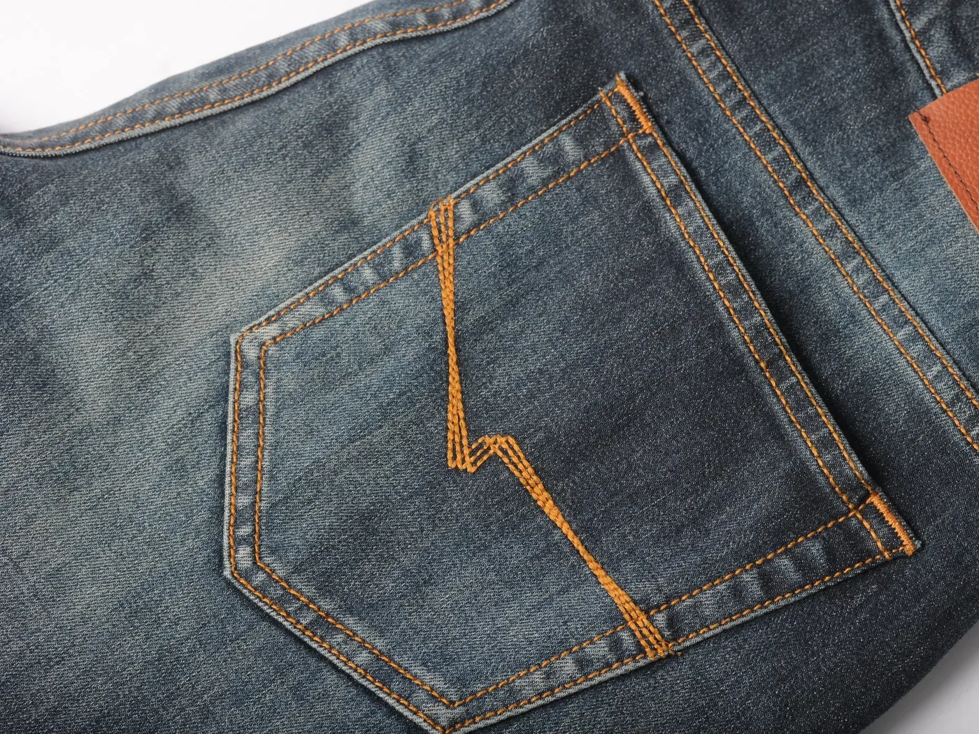 Detail kantong belakang jeans dengan label kulit dan jahitan kontras